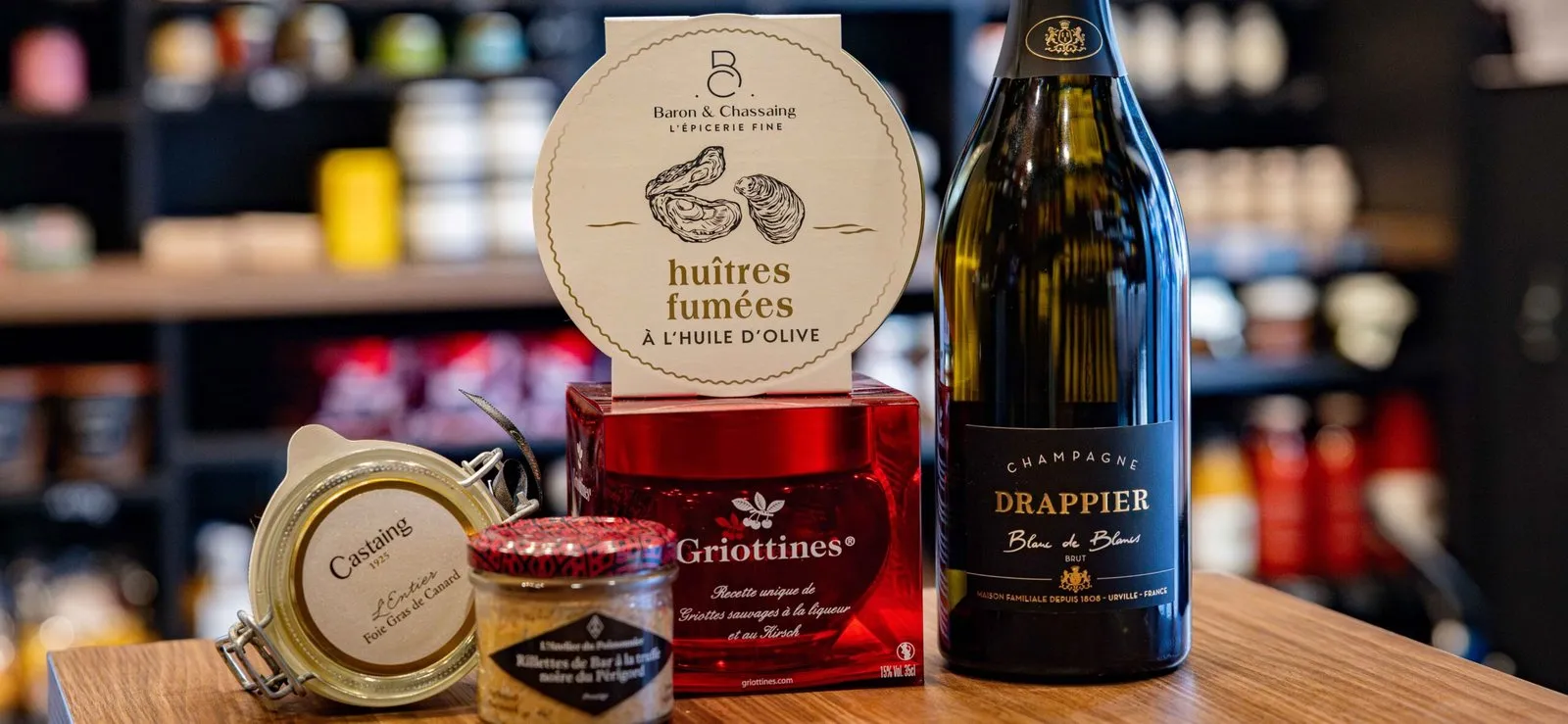 Smoked oysters, griottines, foie gras, rillettes and a bottle of Drappier champagne on the shop counter, with stocked shelves behind